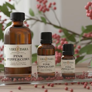 May include: Three amber glass bottles of essential oil with black caps, labeled "Viri Dara Pink Peppercorn." The bottles are arranged on a clear tray with scattered pink peppercorns and a backdrop of red berries.