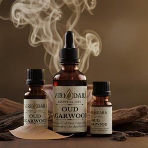 May include: Three amber glass bottles of essential oils with black caps, labeled "Viri Dara Oud Agarwood." The bottles are arranged on a wooden surface with a leaf and wood pieces. Wisps of smoke rise in the background.