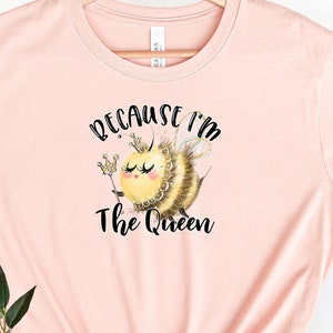 May include: A light pink t-shirt with a graphic of a bee wearing a crown and holding a scepter. The text "Because I'm The Queen" is printed below the bee.