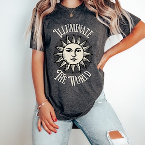 May include: A dark gray t-shirt with a vintage-style sun graphic and the text "Illuminate the World".