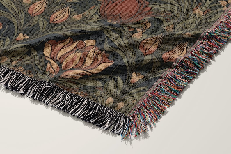 Pu&ograve; includere: Una coperta in tessuto intrecciato con uno sfondo verde scuro e un motivo floreale in tonalit&agrave; di marrone, rosso e crema. La coperta ha un bordo a frangia.