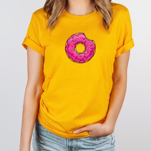May include: A yellow t-shirt with a pink and white donut graphic. The donut has sprinkles and a bite taken out of it.
