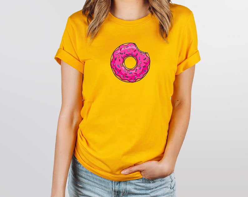 May include: A yellow t-shirt with a pink and white donut graphic. The donut has sprinkles and a bite taken out of it.