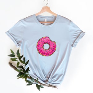 May include: A light blue t-shirt with a pink donut with sprinkles and a bite taken out of it.
