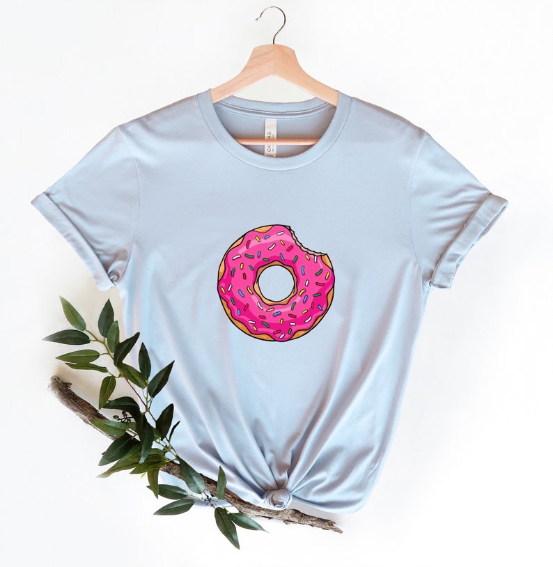 May include: A light blue t-shirt with a pink donut with sprinkles and a bite taken out of it.