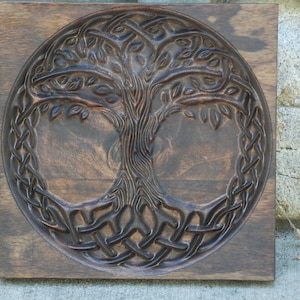 May include: A dark brown wooden wall plaque with a carved tree of life design. The tree has intricate branches and roots, and is surrounded by a Celtic knot pattern.