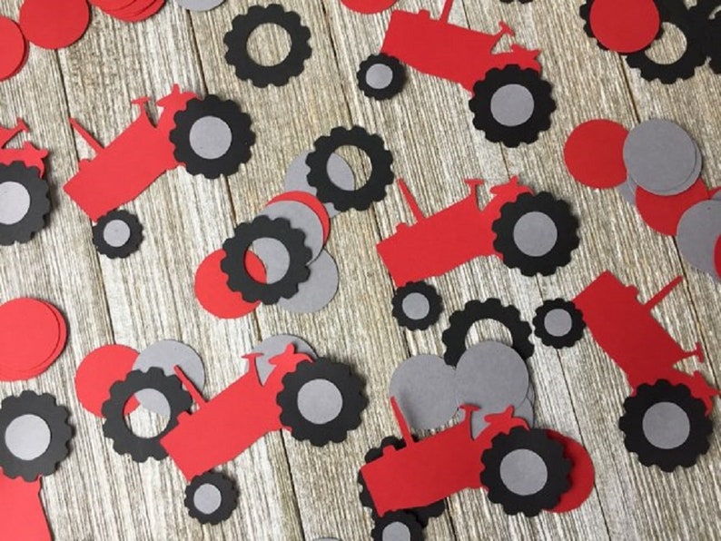 May include: Red and gray paper cutouts of tractors with wheels. The tractor cutouts are scattered on a woodgrain surface.
