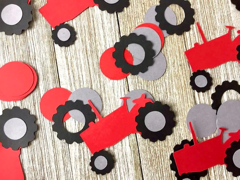 May include: Red and black paper cutouts of tractors with gray wheels. The cutouts are scattered on a wooden surface.