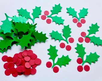 May include: A pile of green paper holly leaves and red paper circles. The holly leaves are in the shape of a traditional holly leaf with three points. The red circles are scattered around the holly leaves.