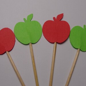 May include: Four paper apple cutouts on wooden sticks. Two apples are red and two are green.