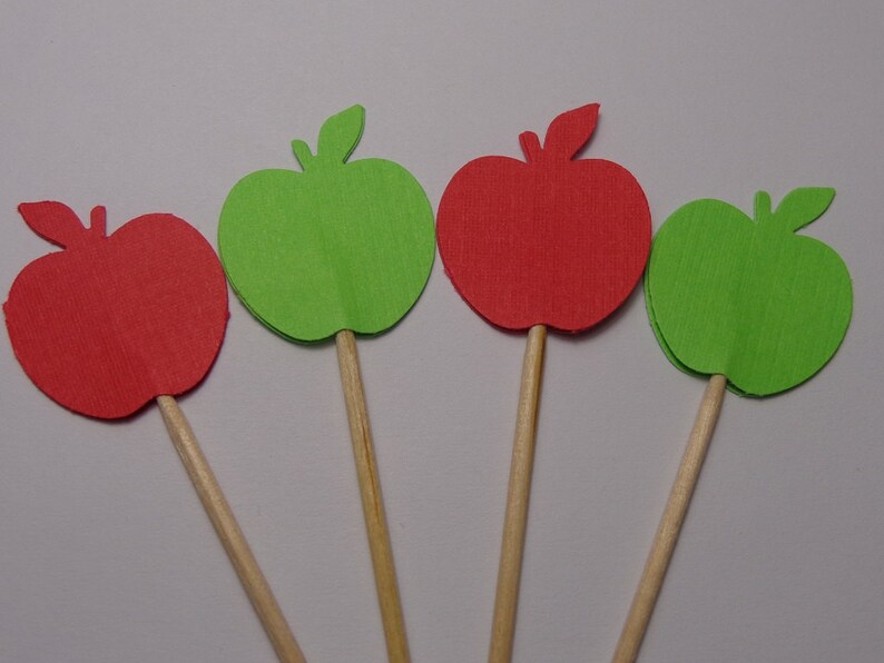 May include: Four paper apple cutouts on wooden sticks. Two apples are red and two are green.