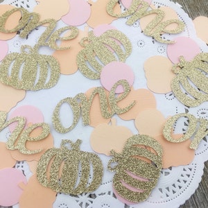 May include: Gold glitter confetti with the word "one" and pumpkin shapes in peach and pink colors.