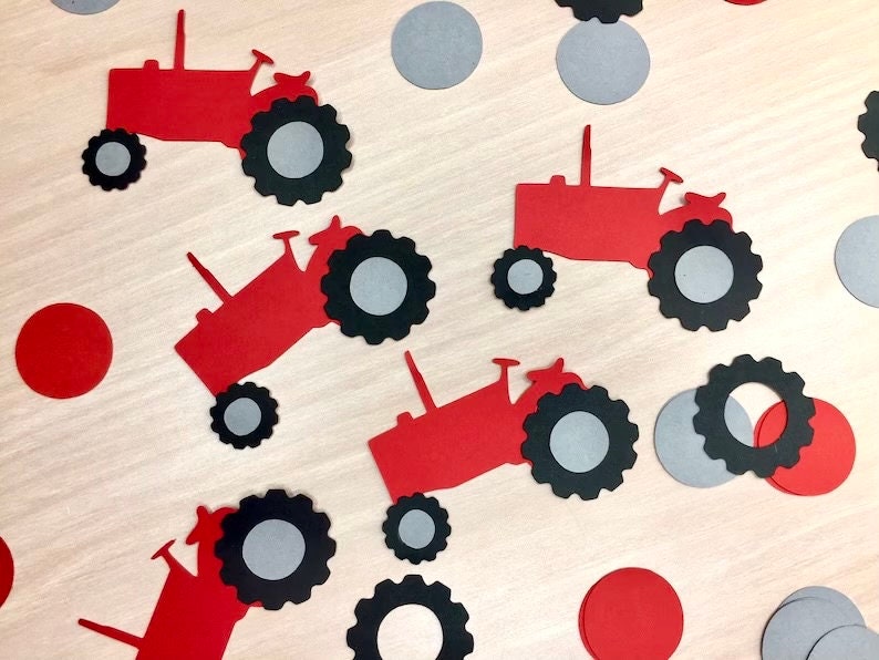 May include: Red and black paper cutouts of tractors with gray circles scattered around them. The tractors have black wheels and red bodies.