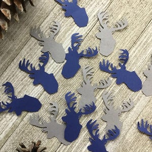 May include: A collection of blue and gray paper deer head cutouts. The deer heads are scattered on a wooden surface.