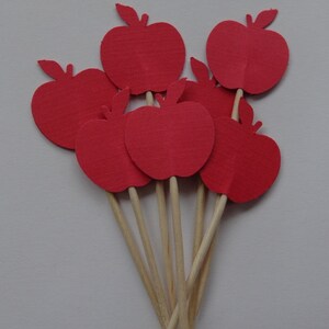 May include: A set of six red paper apple cupcake toppers on wooden sticks. The apples are all the same size and shape, and they are arranged in a cluster.