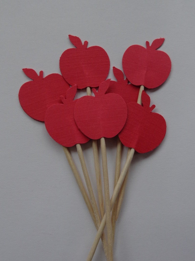 May include: A set of six red paper apple cupcake toppers on wooden sticks. The apples are all the same size and shape, and they are arranged in a cluster.