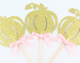 Peut inclure: Trois décorations de gâteau en forme de citrouille à paillettes dorées, chacune présentant une découpe avec une tige bouclée. Un nœud en ruban de satin rose pâle est attaché à la base de chaque citrouille, fixée sur un pic en bois pointu.