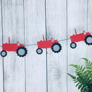 K&ouml;nnte beinhalten: Rote und graue Papier-Traktor-Ausschnitte, die zu einem Banner zusammengef&uuml;gt sind. Das Banner h&auml;ngt vor einem wei&szlig;en Holz Hintergrund.
