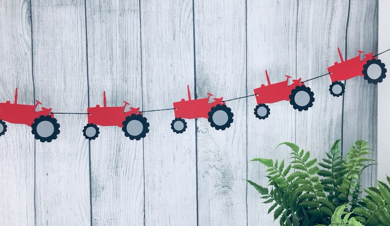 K&ouml;nnte beinhalten: Rote und graue Papier-Traktor-Ausschnitte, die zu einem Banner zusammengef&uuml;gt sind. Das Banner h&auml;ngt vor einem wei&szlig;en Holz Hintergrund.