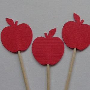 May include: Three red paper apple cutouts on wooden sticks. The apples are a simple silhouette shape with a leaf on top.