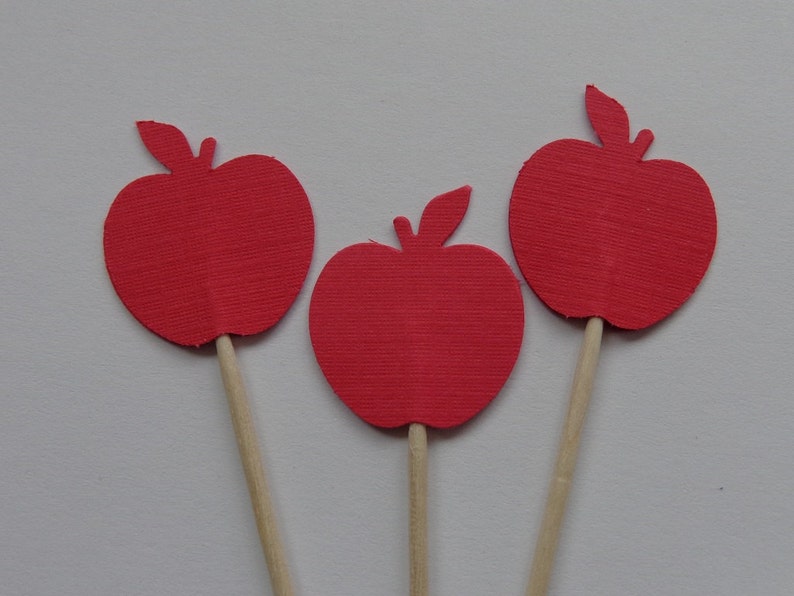 May include: Three red paper apple cutouts on wooden sticks. The apples are a simple silhouette shape with a leaf on top.