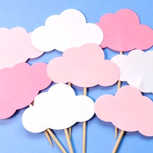 May include: A set of nine pink and white cloud-shaped paper cupcake toppers. The toppers are attached to wooden skewers.