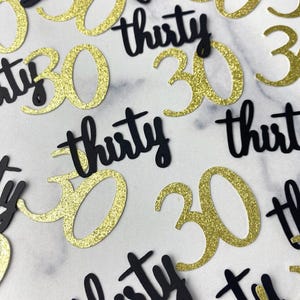 May include: A collection of scattered confetti pieces featuring the number 30 in gold glitter and the word thirty in a black matte finish. The pieces are arranged in a random pattern, showcasing the contrasting textures of the shiny gold and black.