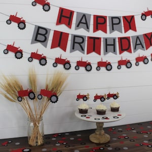 May include: Red and gray tractor themed birthday party decorations. A banner reads "Happy Birthday" with red and gray pennants and red tractors. There are also red tractor cupcake toppers and red and gray confetti.