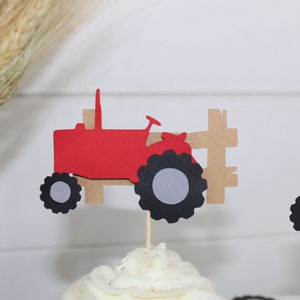 K&ouml;nnte beinhalten: Roter und schwarzer Traktor-Cupcake-Topper mit einem braunen Holzzaun. Der Traktor hat ein graues Rad und einen schwarzen Reifen.