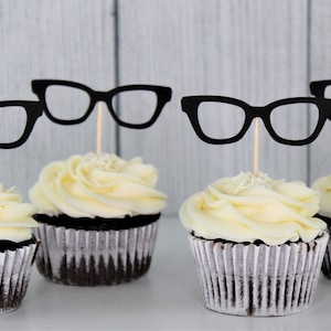 May include: Four chocolate cupcakes with white frosting and black paper glasses toppers.