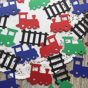 Puede incluir: Surtido de recortes de papel de trenes y vías en rojo, azul, verde y negro. Los recortes de trenes tienen ruedas y una chimenea. Los recortes de vías son negros y tienen un diseño simple.