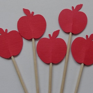 May include: Five red paper apple cutouts on wooden sticks. The apples are all the same size and shape, and they are arranged in a semi-circle.