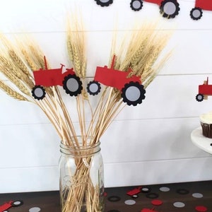 K&ouml;nnte beinhalten: Rote und schwarze Traktor-Papierschnitte auf St&ouml;cken in einer Vase mit Weizen&auml;hren. Rote und schwarze Traktor-Cupcake-Topper auf Cupcakes auf einem Kuchenst&auml;nder mit roten und grauen Konfetti.
