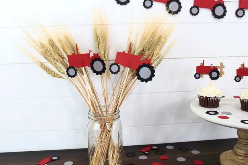 K&ouml;nnte beinhalten: Rote und schwarze Traktor-Papierschnitte auf St&ouml;cken in einer Vase mit Weizen&auml;hren. Rote und schwarze Traktor-Cupcake-Topper auf Cupcakes auf einem Kuchenst&auml;nder mit roten und grauen Konfetti.