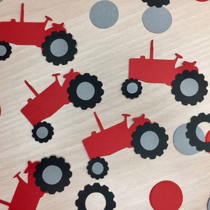 May include: Red and black paper cutouts of tractors with gray wheels. The cutouts are scattered on a wooden surface with red and gray paper circles.