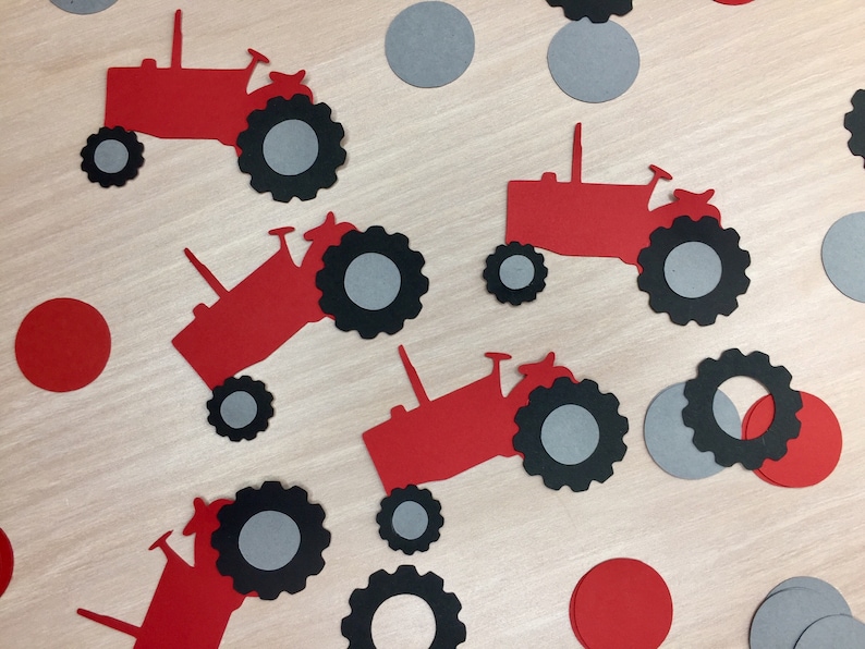 May include: Red and black paper cutouts of tractors with gray wheels. The cutouts are scattered on a wooden surface with red and gray paper circles.