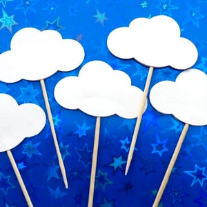 Op de afbeelding: Vijf witte cupcake-toppers in de vorm van een wolk met houten stokjes. De toppers zijn tegen een blauwe achtergrond met witte sterren.