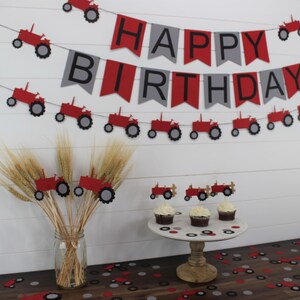 May include: Red and gray tractor themed birthday party decorations. A banner reads "Happy Birthday" with red and gray pennants and red tractors. There are also red tractor cupcake toppers and red and gray confetti.
