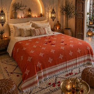 Peut inclure: Scène de chambre avec un plaid orange à motifs sur un lit, complété par des coussins décoratifs. Le lit repose sur un tapis à motifs, avec une table de chevet et des lanternes suspendues. La pièce dégage une ambiance chaleureuse.