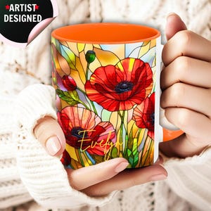 May include: A ceramic mug with an orange interior and a stained glass style floral pattern featuring red poppies and green stems. The name Evelyn is written in gold cursive script on the front. A circular sticker reads Artist Designed.