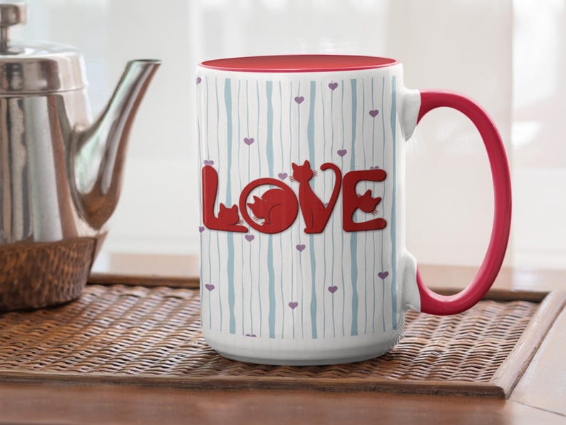 May include: White ceramic mug with a red interior and handle. The mug features the word "LOVE" in red, with cat silhouettes replacing the letters. The mug has a striped pattern with small purple hearts.