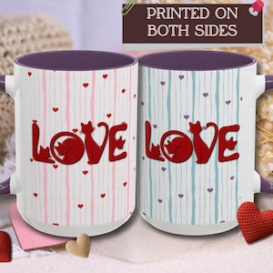 May include: Two white ceramic mugs with purple handles and interiors. Each mug features the word "LOVE" in red, with a cat silhouette replacing the "O". The mugs have vertical striped patterns in pink and blue, with small heart accents. The text "PRINTED ON BOTH SIDES" is at the top.