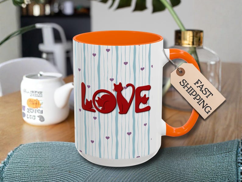 May include: White ceramic mug with an orange interior and handle. The mug features the word "LOVE" in red with cat silhouettes, and a pattern of blue vertical lines and purple hearts. A tag reads "FAST SHIPPING".