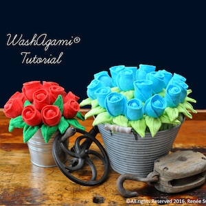 Peut inclure: Deux bouquets de roses en tissu dans des seaux en métal galvanisé. Un bouquet est rouge et l'autre est bleu. Les bouquets sont sur une surface en bois avec une poulie vintage et une roue en métal.