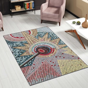 May include: A rectangular area rug with a mosaic design. The rug features a central sunburst pattern in shades of beige, red, blue, and gray. The mosaic design is composed of small, square tiles, creating a textured appearance. The rug is placed on a light-colored wooden floor.