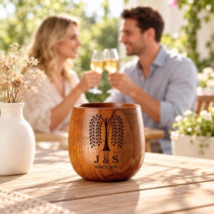 May include: A rounded wooden cup featuring a dark brown engraved willow tree graphic above the text J & S and SINCE 2011. The cup has a smooth, polished finish with visible wood grain patterns, standing on a slatted wooden surface.