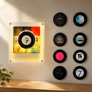 May include: A square, illuminated wall display featuring a central vinyl record graphic with a hot air balloon design, surrounded by eight smaller circular wall-mounted vinyl record discs displaying various album art and logos including BTS and Wings.