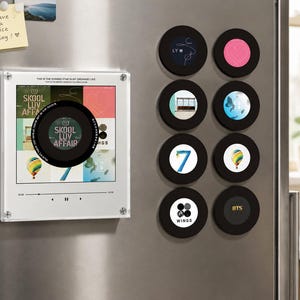 May include: A square acrylic display frame featuring a music player interface with the text Skool Luv Affair and eight circular magnets with various graphic designs including the number 7, a hot air balloon, and the BTS logo attached to a metal surface.