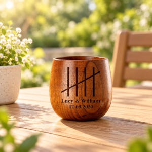 May include: A rounded wooden cup featuring a dark brown grain and a laser-engraved tally mark design. Below the tally marks, the text reads Lucy & William followed by the date 12.09.2020. The cup has a smooth, curved exterior surface.