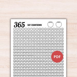May include: A white printable sheet featuring a 365 day countdown tracker with numbered circles from 1 to 365 arranged in rows. The header displays the text 365 DAY COUNTDOWN with two empty circles labeled Event and Date. A red PDF icon is visible.
